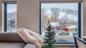 Una habitación con un amplio ventanal que da a una calle nevada y un árbol de Navidad decorado.