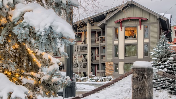 Un edificio de varios pisos con balcones, un paisaje nevado y un árbol de Navidad con luces.