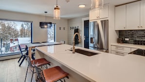 Una cocina moderna con una isla grande, electrodomésticos de acero inoxidable e iluminación colgante.