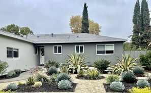 A two-story house with a grey exterior, a covered patio, and a garden with various succulents and cacti.