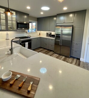 A modern kitchen with grey cabinets, stainless steel appliances, and a white countertop.