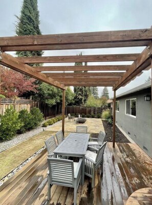 A wooden pergola structure in a backyard with a patio table and chairs.