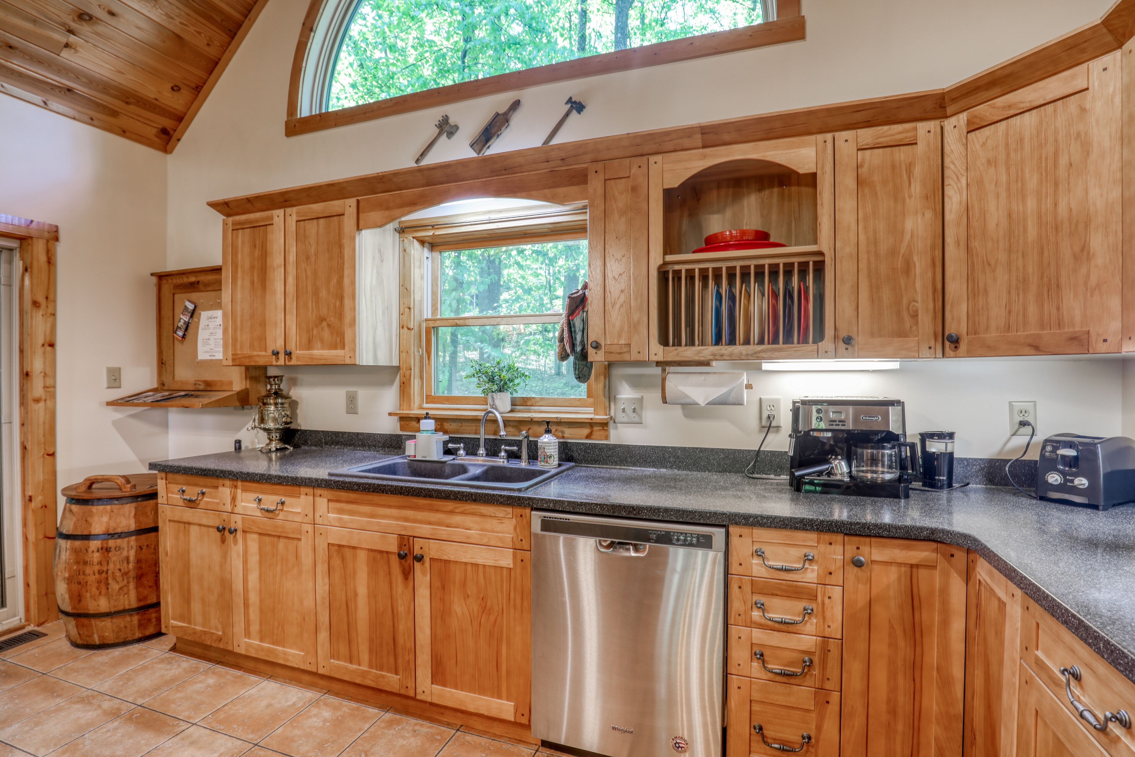 A kitchen with wooden cabinets, a dishwasher, a coffee maker, and a window with a view of trees.