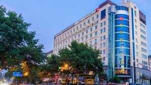 Ein mehrgeschossiges Hotel mit einer auffälligen, geschwungenen Glasfassade, einem roten Logo in der Ecke und einem Schild, das es als Hotel kennzeichnet.