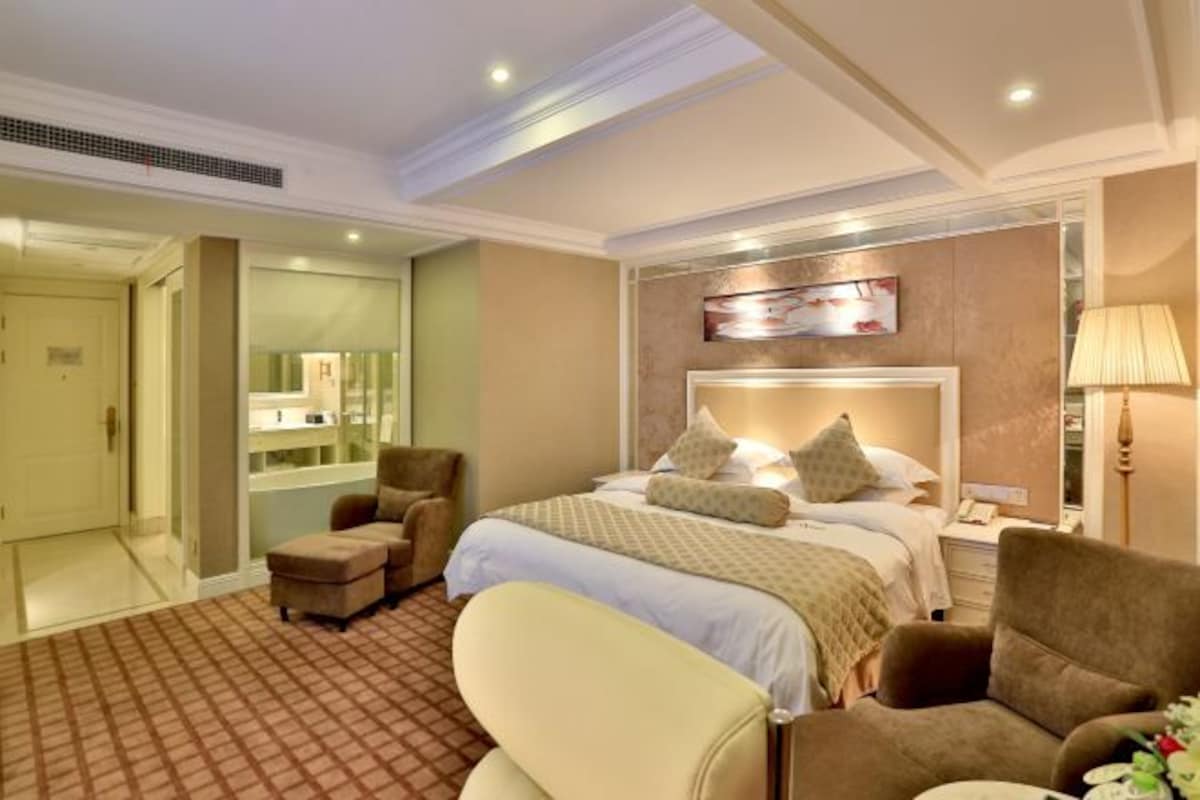 Ein Hotelzimmer mit einem großen Bett, zwei Sesseln, einem kleinen Tisch und einem Spiegel.