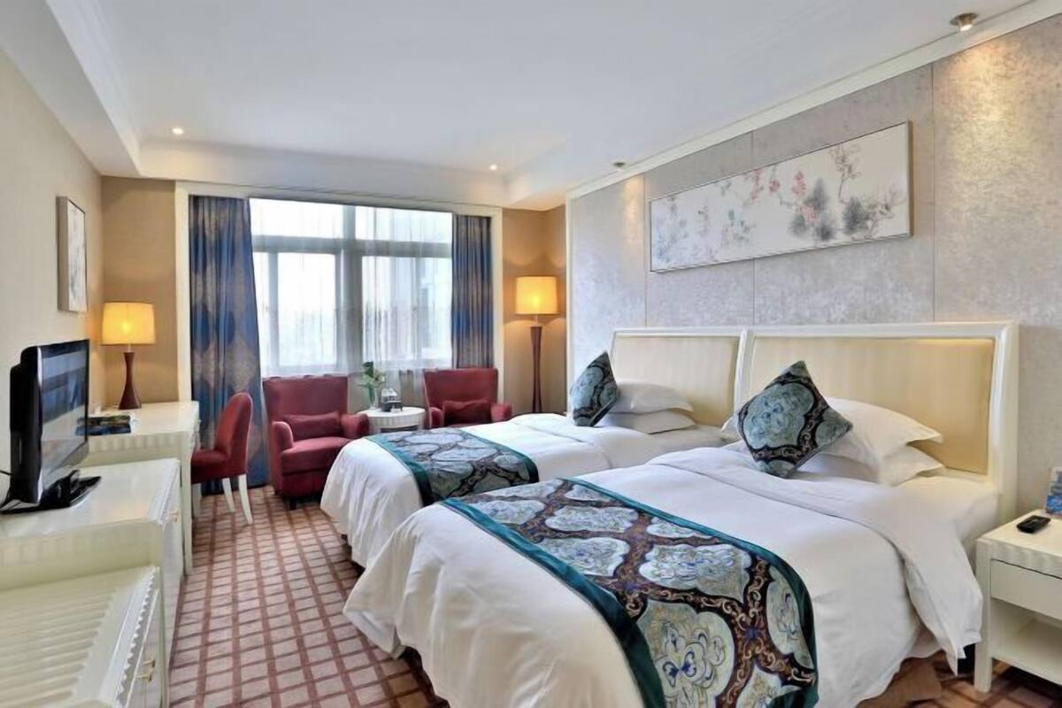 Une chambre d’hôtel avec deux lits, un bureau avec une télévision, une chaise et une fenêtre avec des rideaux.
