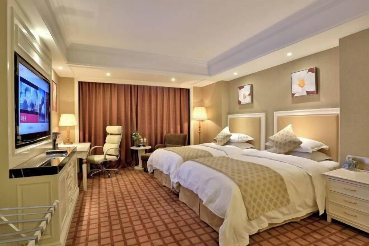 Une chambre d’hôtel équipée d’une télévision, de deux lits, d’un bureau, d’une chaise et d’une petite table.
