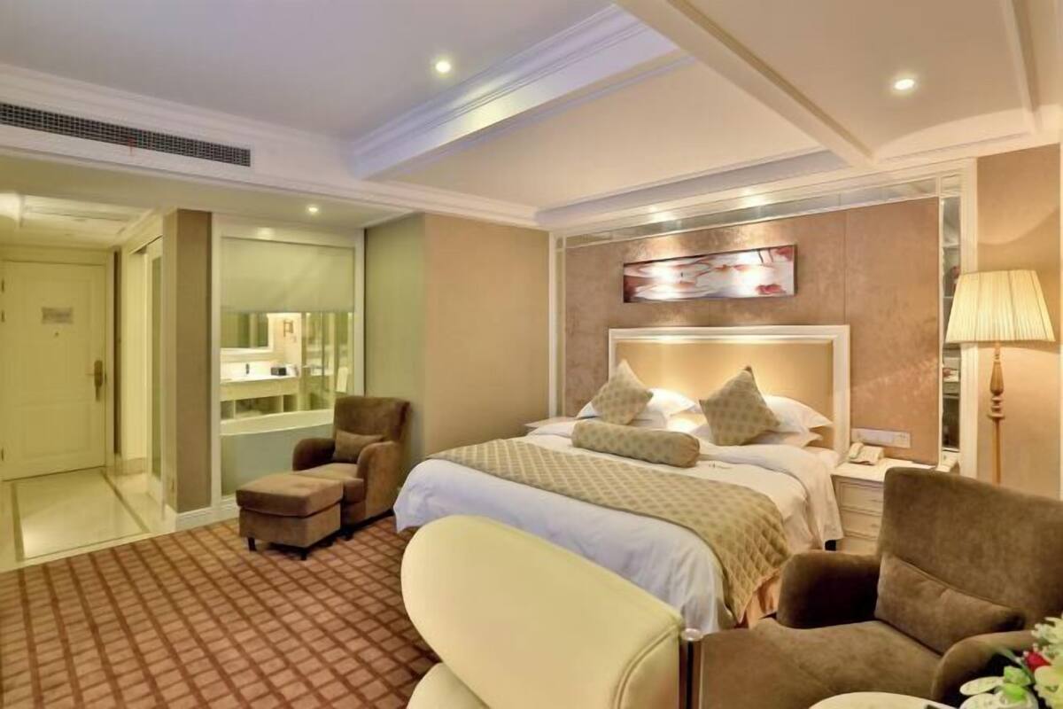 Une chambre d’hôtel avec un lit, deux fauteuils, un bureau et un miroir.