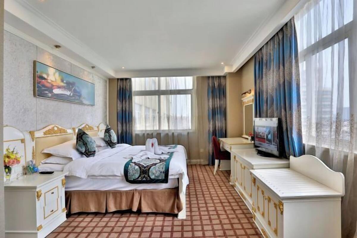 Une chambre d’hôtel équipée d’un lit, d’une table de chevet, d’une télévision, d’un bureau et de grandes fenêtres.