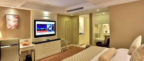 Habitación de hotel con cama, escritorio, televisor y baño visible a través de una puerta abierta.