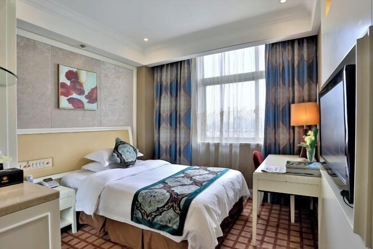 Een hotelkamer met een bed, een bureau, een televisie en een raam met gordijnen.