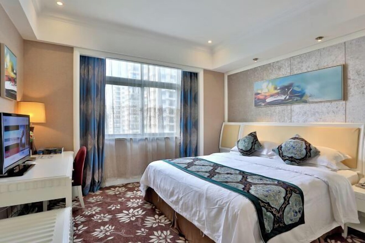 Een hotelkamer met een bed, een bureau, een televisie en een schilderij aan de muur.