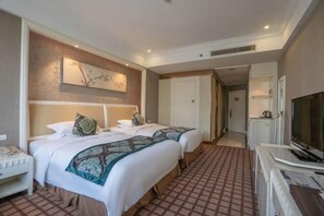 Ein Hotelzimmer mit zwei Betten, einem Schreibtisch, einem Telefon, einem Fernseher und einem Bild an der Wand.