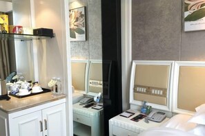 Een hotelkamer met een bed, nachtkastje en een spiegel. Daarboven, boven het bed, bevindt zich een plank met diverse voorwerpen.