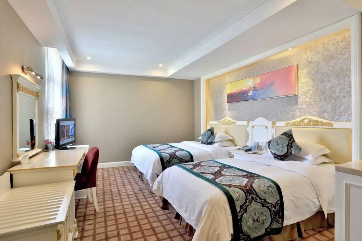 Une chambre d’hôtel avec deux lits, un bureau, une chaise, une télévision et un tableau au mur.