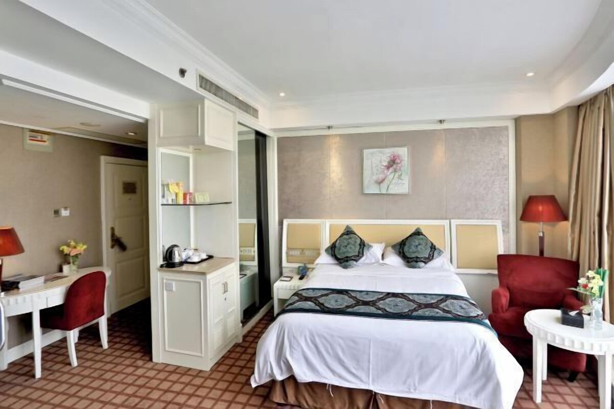 Een hotelkamer met een bed, een bureau, een stoel, een klein tafeltje en een rode fauteuil.