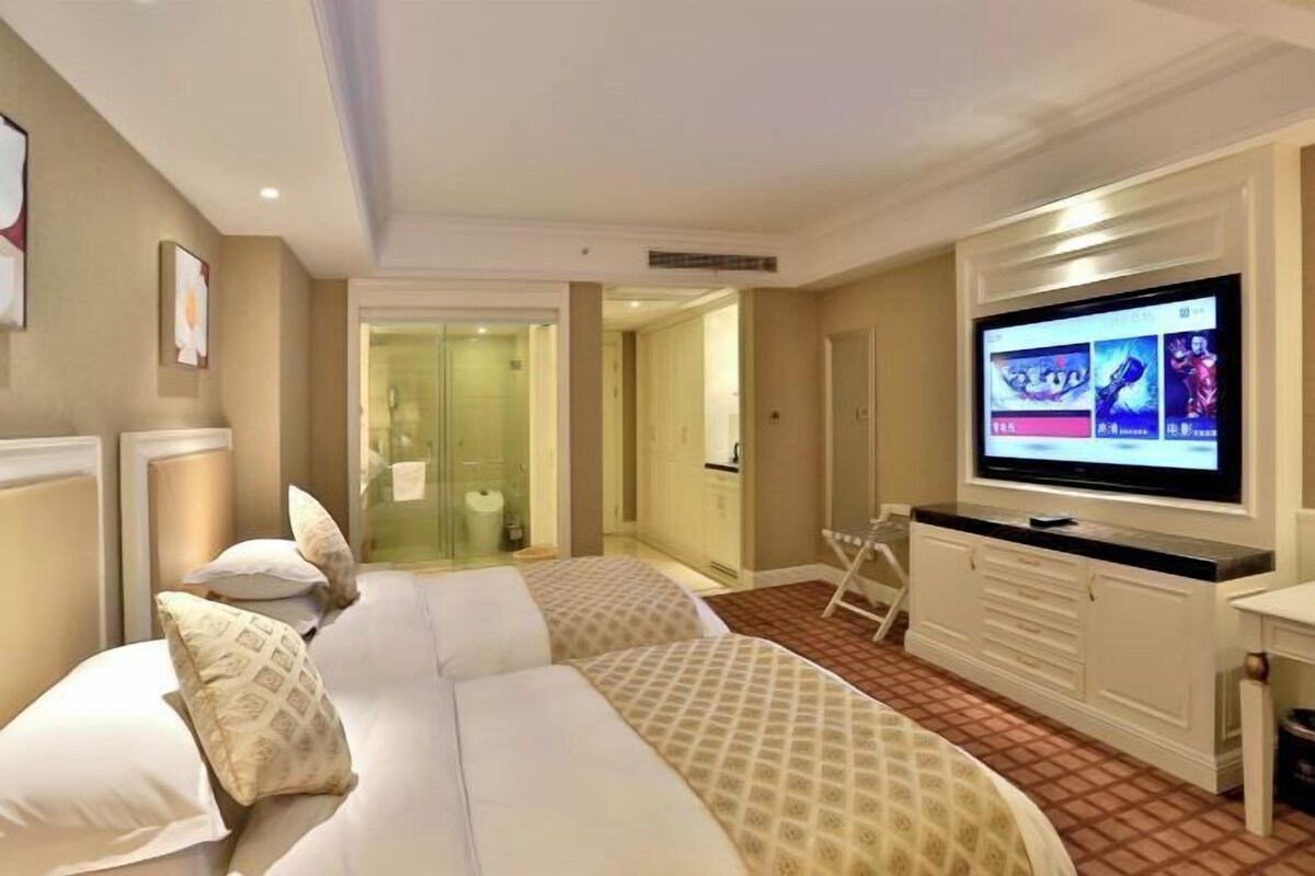 Een hotelkamer met een groot bed, een televisie en een badkamer die zichtbaar is door een glazen deur.