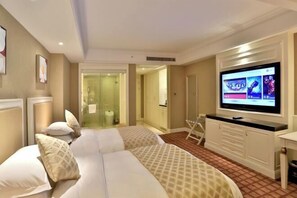 Een hotelkamer met een groot bed, een televisie en een badkamer die zichtbaar is door een glazen deur.