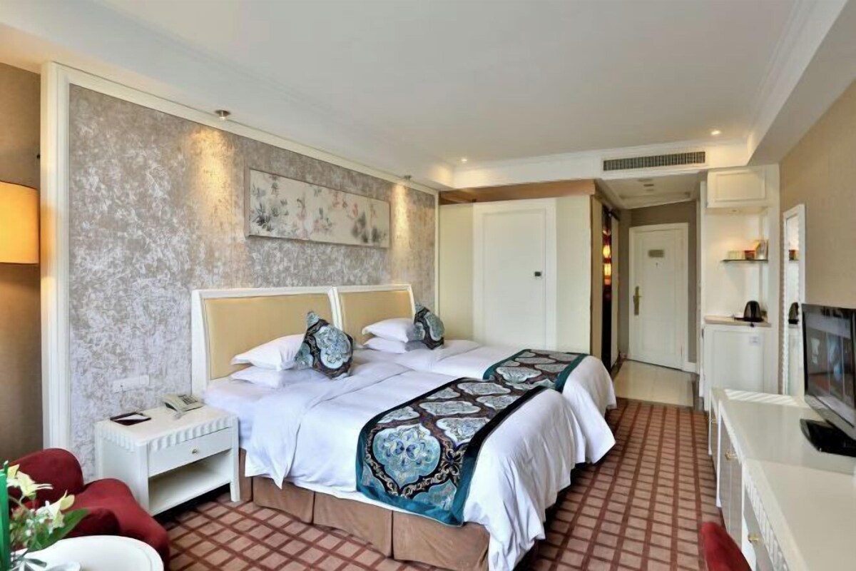 Een hotelkamer met een groot bed, nachtkastjes, een bureau met een televisie en een schilderij aan de muur.