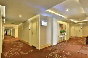 A hotel corridor with carpeted flooring, doors, and a small table with a plant. - Zhong'an Huana Holiday Hotel (Hangzhou)