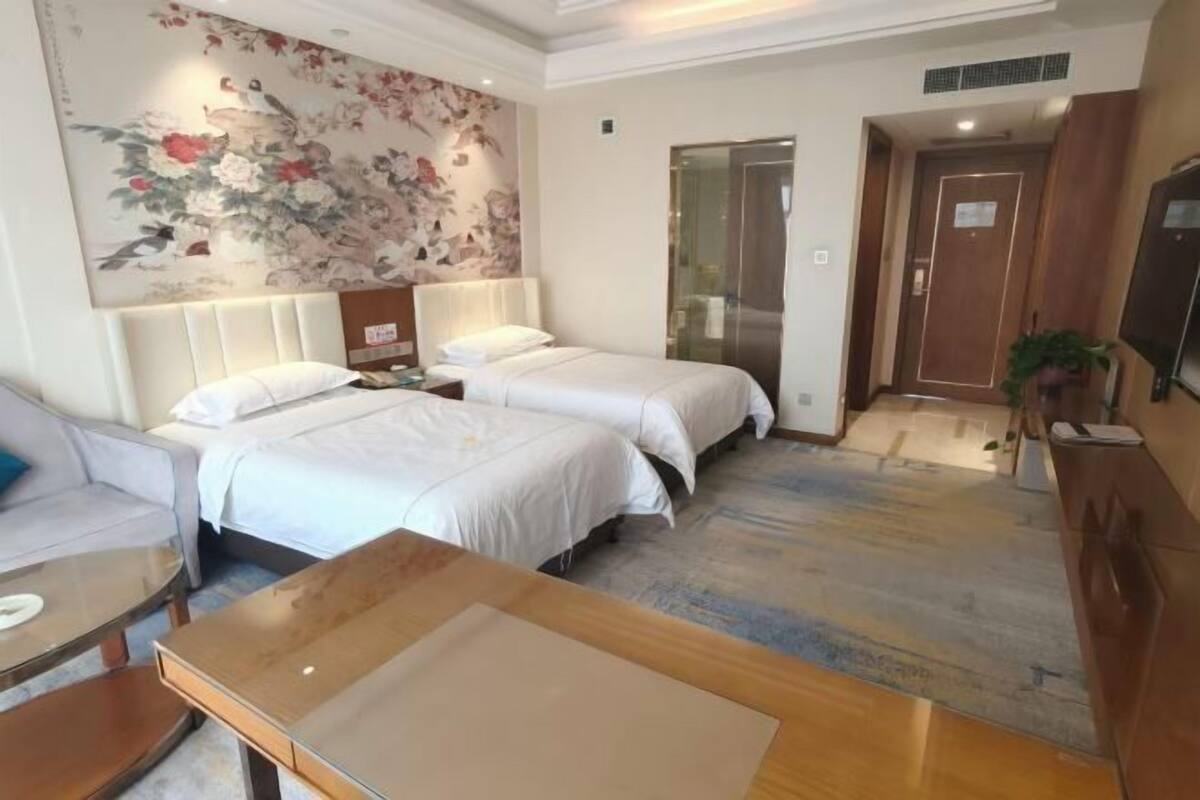 Habitación de hotel con dos camas, un sofá, una mesa de madera, un mural floral en la pared y un televisor.