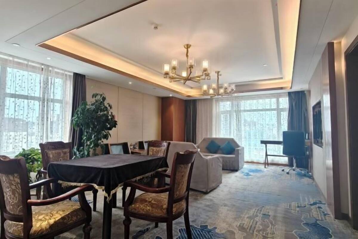 Un salón de conferencias de hotel con una mesa redonda, sillas, una araña y ventanas amplias.