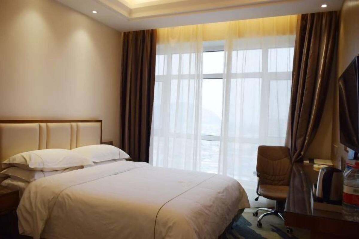 Una habitación de hotel con cama, una silla, un escritorio y un ventanal con cortinas.