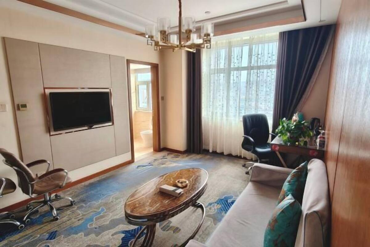 Una habitación de hotel con un televisor de pantalla plana grande, un sofá, una mesa de centro y un escritorio con una silla.