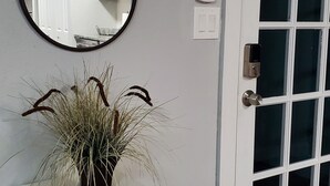 A white console table with a mirror and a potted plant, a door with a keypad lock, and a window with frosted glass panels. - Coastal Home w/ Outdoor Living, 10 min to Beach (Vero Beach)
