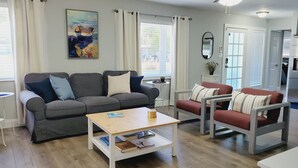 A modern living room with a grey sofa, a red armchair, a small wooden coffee table, and a painting on the wall. - Coastal Home w/ Outdoor Living, 10 min to Beach (Vero Beach)