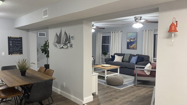 A modern living room with a grey sofa, a wooden dining table, and a small side table. - Coastal Home w/ Outdoor Living, 10 min to Beach (Vero Beach)