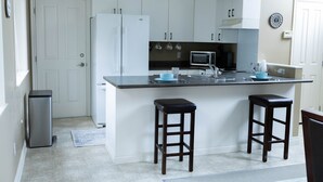 A kitchen with white cabinets, a stainless steel refrigerator, a microwave, and two bar stools. - Quiet, cozy 1 bedroom suite, w/ separate entrance. Now with A/C! (North Saanich)