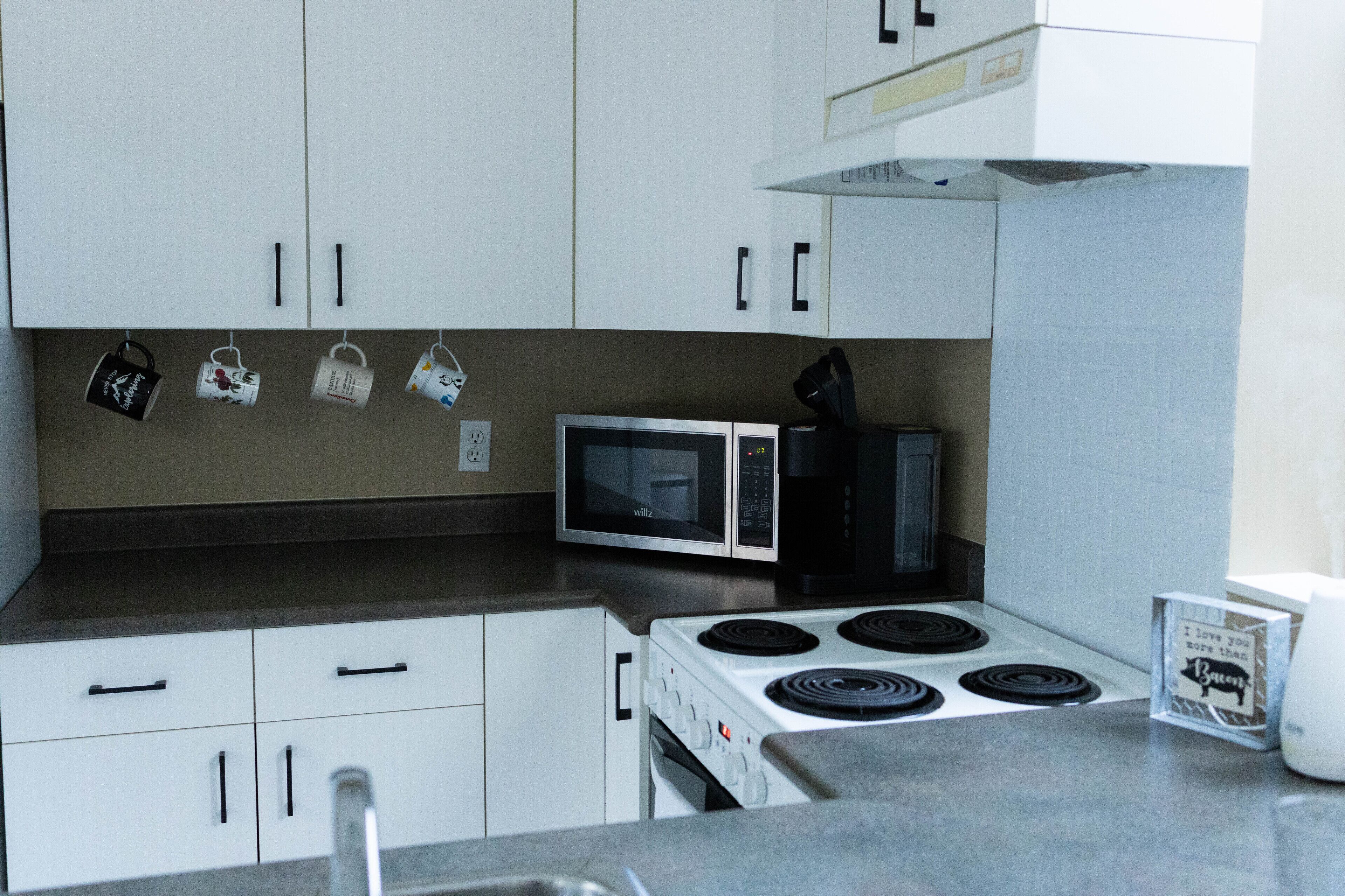 Una cocina con armarios blancos, microondas, estufa y cafetera.