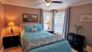 Ein Schlafzimmer mit einem Bett, zwei Nachttischlampen, einem Deckenventilator, einem Nachttisch, einer Kommode und einem Fenster mit Vorhängen.