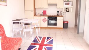 A compact kitchen with white cabinets, a microwave, and a red trash bin. - DINARD - LA RICHARDAIS T2- NEAR SEA AND RANCE (La Richardais)