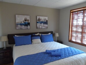 A bedroom with a bed, two wall-mounted paintings, a window with blinds, and a nightstand with a lamp. - Cherry Lane Self Catering in Bloemfontein Family Apartment for max 8 Guests (Bloemfontein)