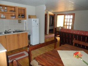 A compact kitchen with wooden cabinets, a white refrigerator, and a dining area with a wooden table and bench. - Cherry Lane Self Catering in Bloemfontein Family Apartment for max 8 Guests (Bloemfontein)