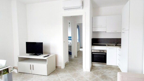 A compact living space with a kitchenette, a TV on a stand, and a dining area. - Blu House a Castelsardo (Castelsardo)