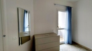 A bedroom with a single bed, a dresser, a mirror, and a window with curtains. - Blu House a Castelsardo (Castelsardo)