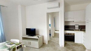 A compact living space with a kitchenette, a dining area with a table and chairs, and a television. - Blu House a Castelsardo (Castelsardo)