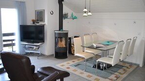 A living room with a TV, fireplace, dining table with chairs, and a sofa. - Two-bedroom Apartment for 4-5 Guests With Lake and Mountain Views (Emmetten)