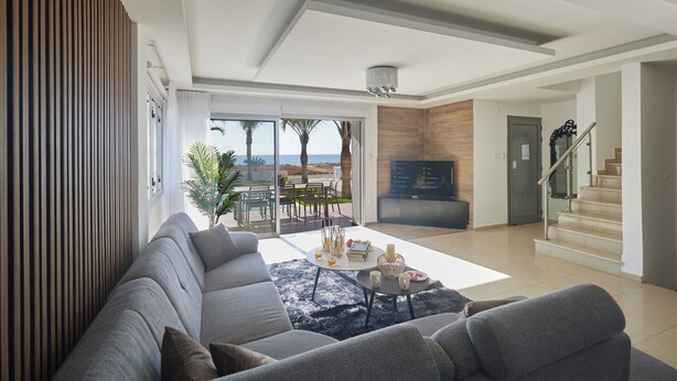 A modern living room with a grey sofa, a coffee table, and a view of the outdoors. - Ayia Napa Holiday Villa Sv9 (Sotira)