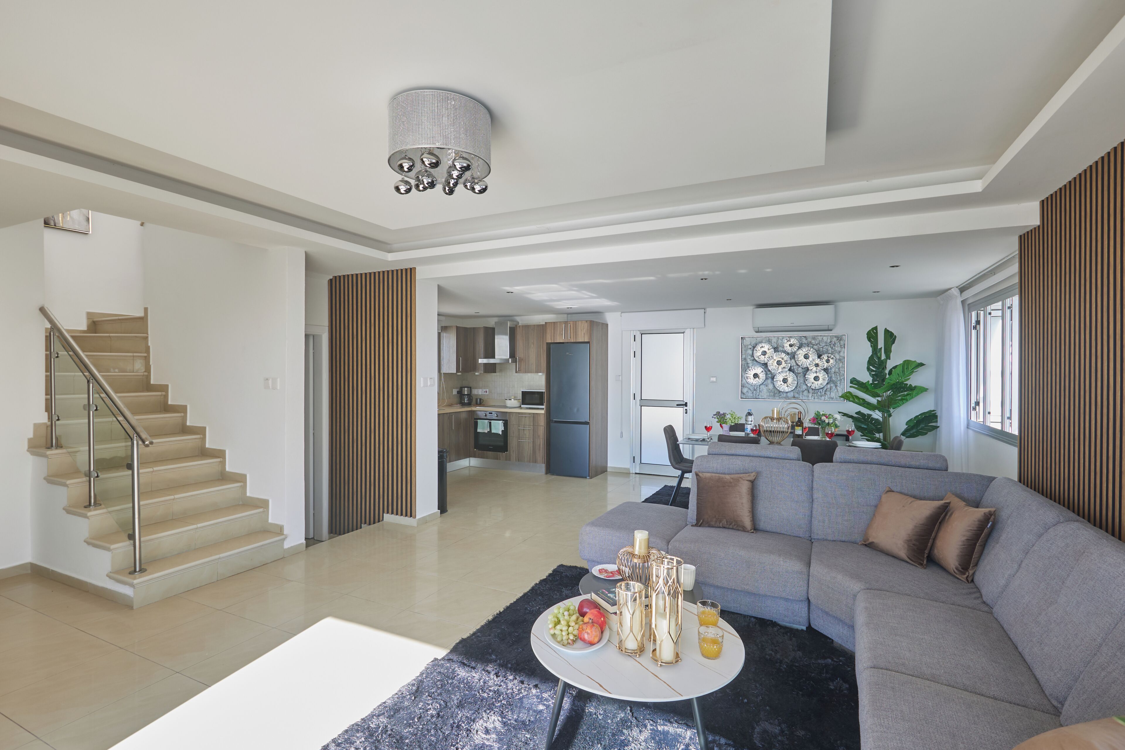 A spacious living area with a grey sofa, a round coffee table, and a staircase leading to another level.