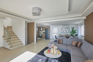 A spacious living area with a grey sofa, a round coffee table, and a staircase leading to another level. - Ayia Napa Holiday Villa Sv9 (Sotira)