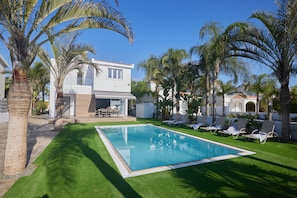 Une piscine entourée de palmiers et un bâtiment blanc doté d’un balcon.