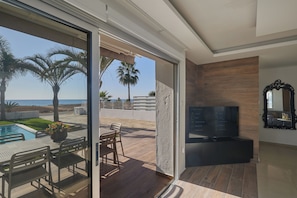 Un salon moderne doté d’un téléviseur, d’un mur recouvert de panneaux en bois et d’une porte vitrée donnant sur un espace piscine aménagé avec du mobilier d’extérieur.
