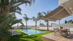 A swimming pool, lounge chairs, a table with chairs, and palm trees. - Ayia Napa Holiday Villa Sv9 (Sotira)