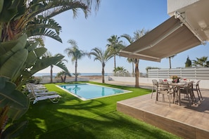 A pool area with artificial grass, lounge chairs, and a table with chairs. - Ayia Napa Holiday Villa Sv9 (Sotira)