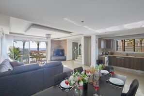 A modern living room with a sofa, dining table set for two, and a kitchen area visible through an open door.