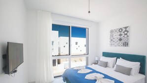Habitación de hotel con cama, televisión, ventana con cortinas y vista a edificios.